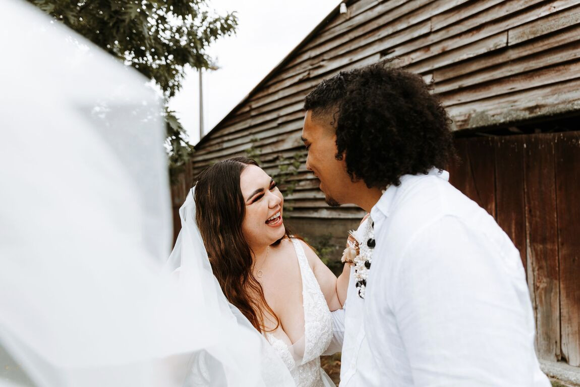 A couple laughing together beside a wooden barn